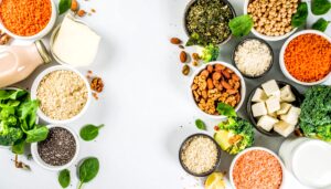 Productos veganos ricos en proteínas: legumbres, quinoa, tofu, leches vegetales y frutos secos dispuestos sobre mesa blanca